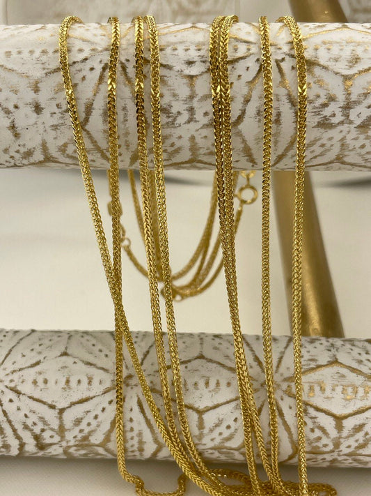 Gold necklaces on a decorative wooden stand with a neutral background
