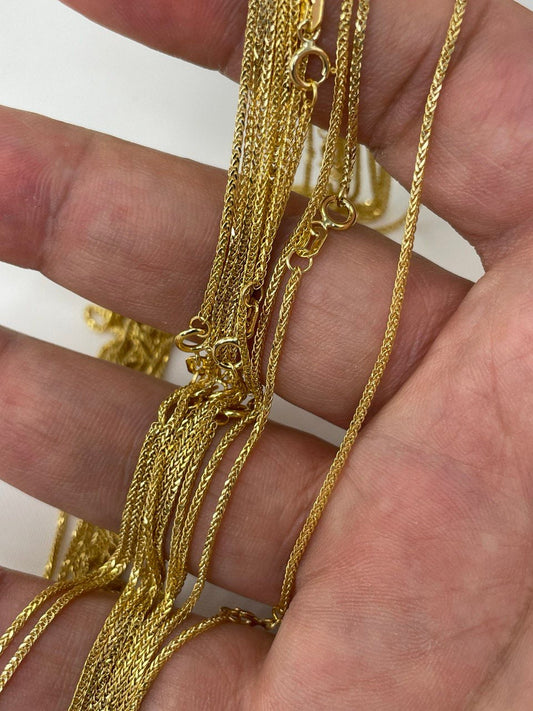 Gold necklaces held in a hand against a white background