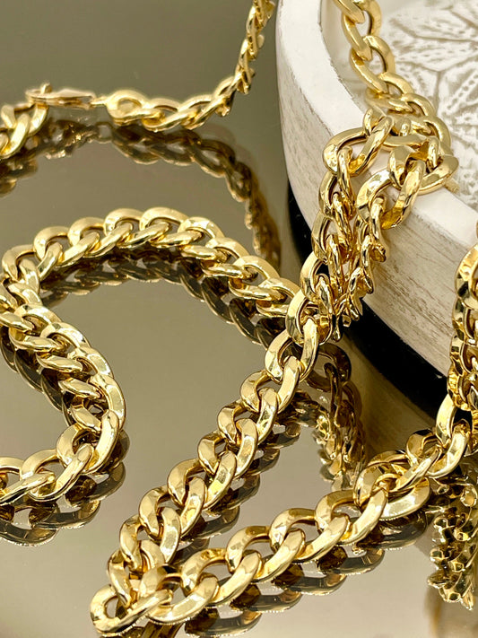 Gold chain necklace on a reflective surface with a white object in the background