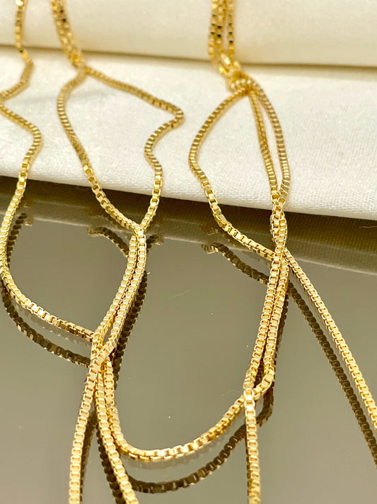 Gold chain necklace on a white cushion with a neutral background