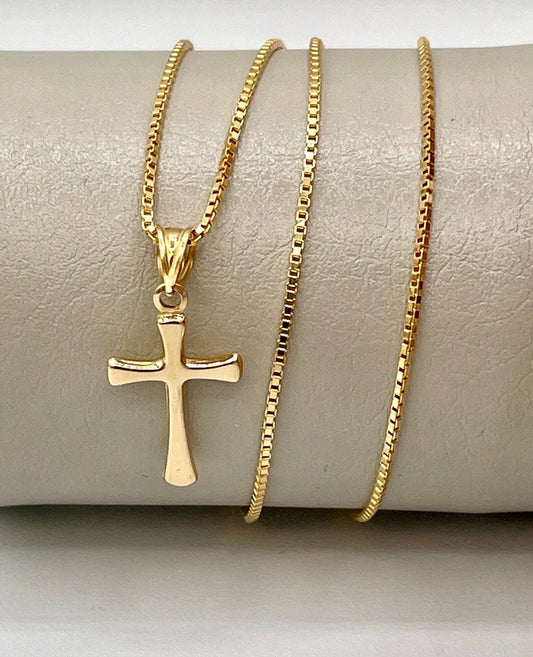 Gold cross pendant necklace on a beige surface