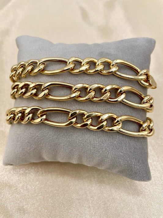 Three gold chain bracelets on a gray pillow against a beige background