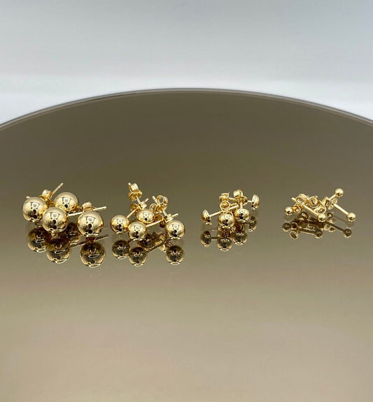 Gold earrings on a reflective surface with a gradient background