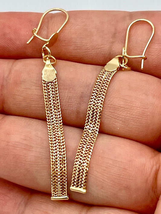 Gold chain earrings held between fingers on a light background