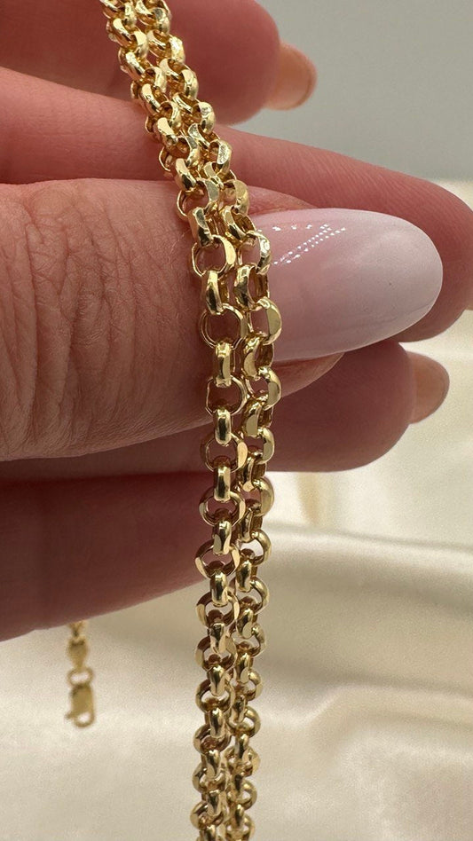Gold chain held between fingers against a neutral background