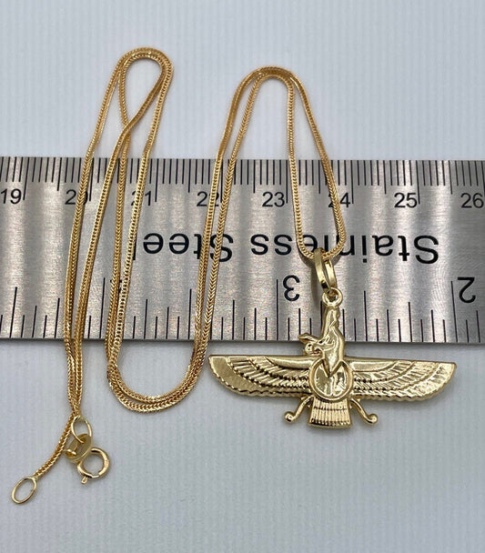 Gold necklace with a winged pendant on a ruler for scale