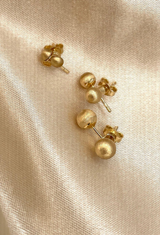 Pair of gold ball earrings on a beige fabric background