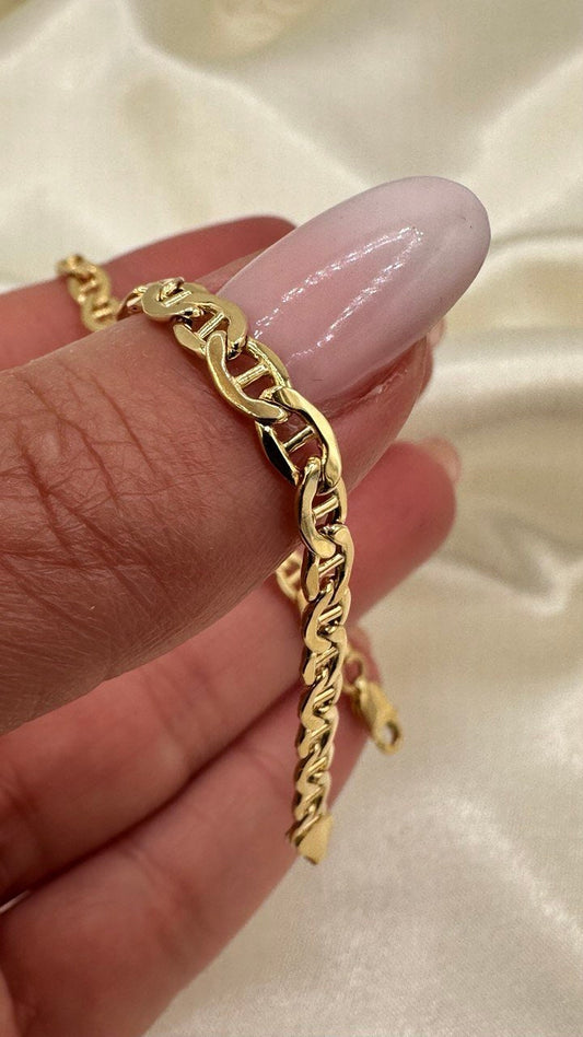 Gold chain bracelet on a hand against a beige background