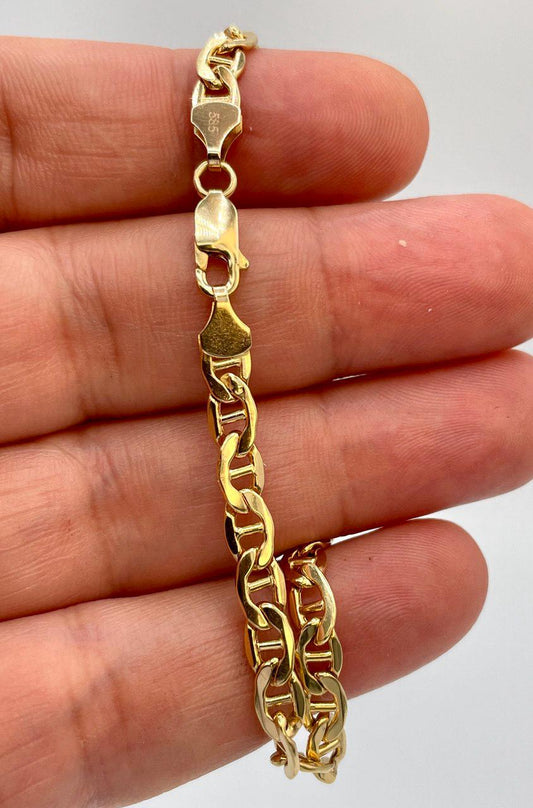 Gold chain bracelet held between fingers against a neutral background