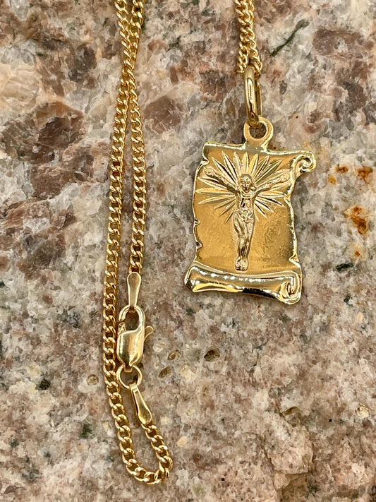 Gold necklace with a religious pendant on a textured surface