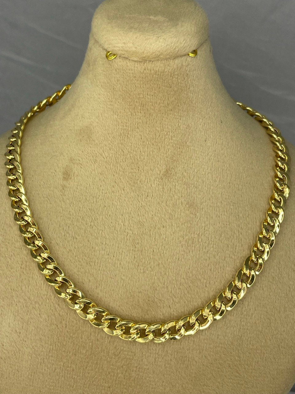 Gold chain necklace on a mannequin bust with a gray background