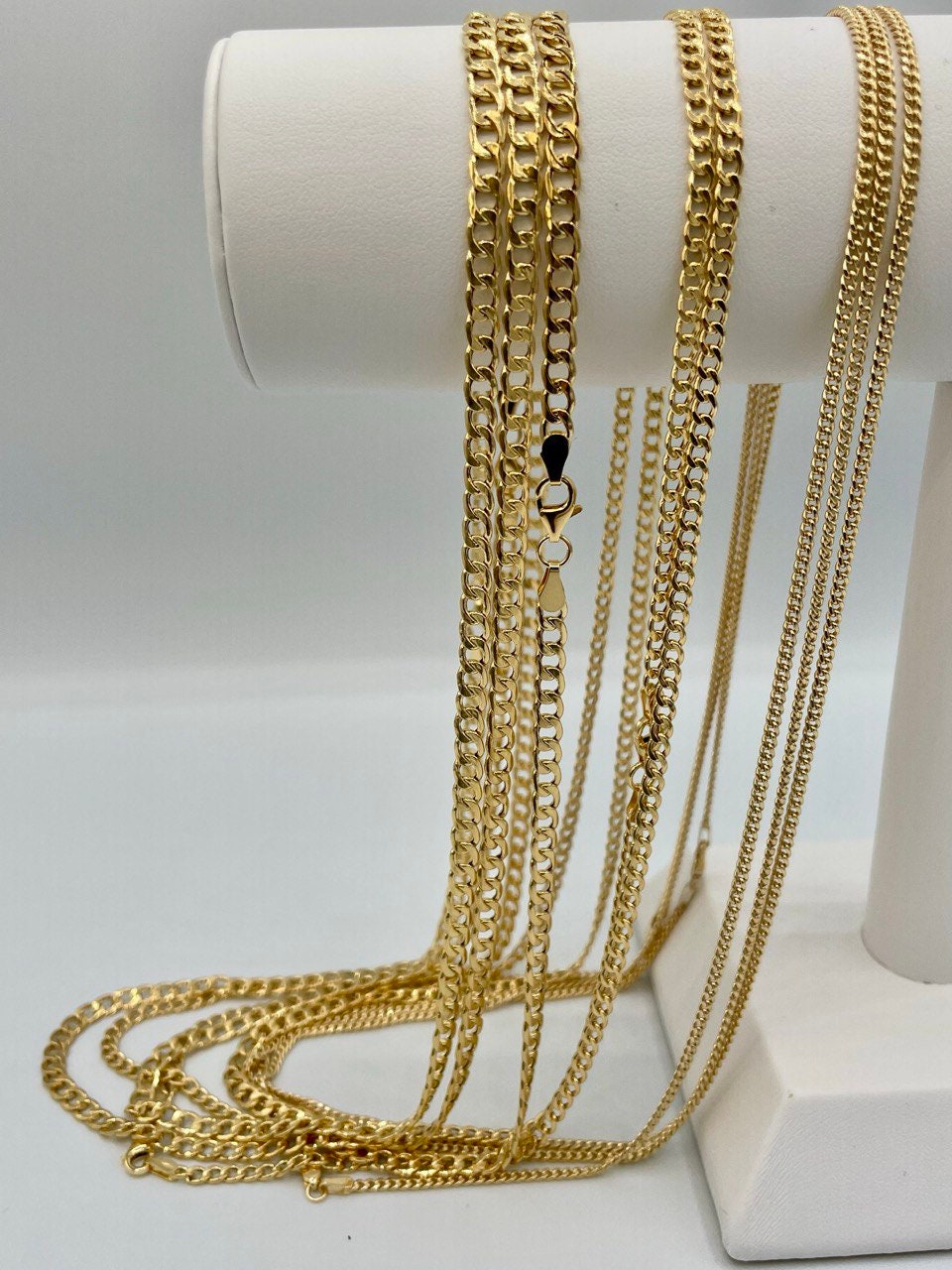 Gold chains displayed on a white cylindrical stand against a light gray background