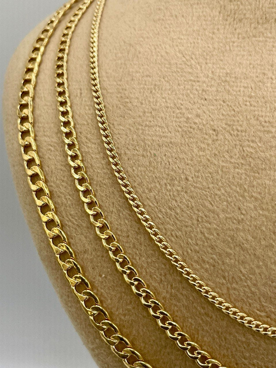 Two gold chains on a beige surface