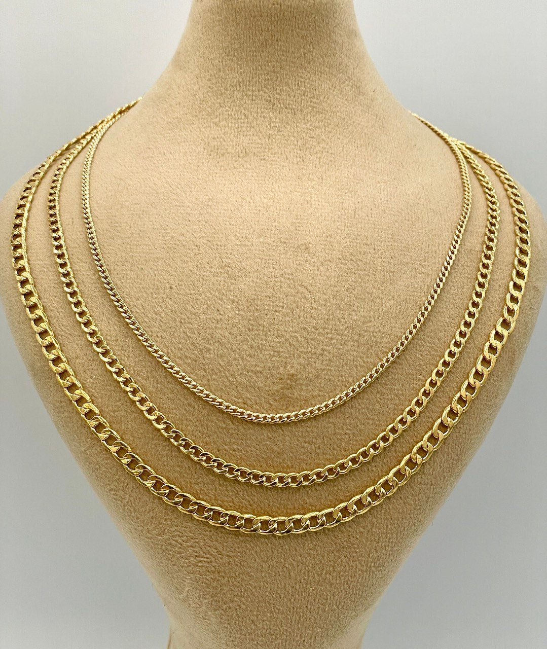 Three gold chains displayed on a mannequin bust against a plain background