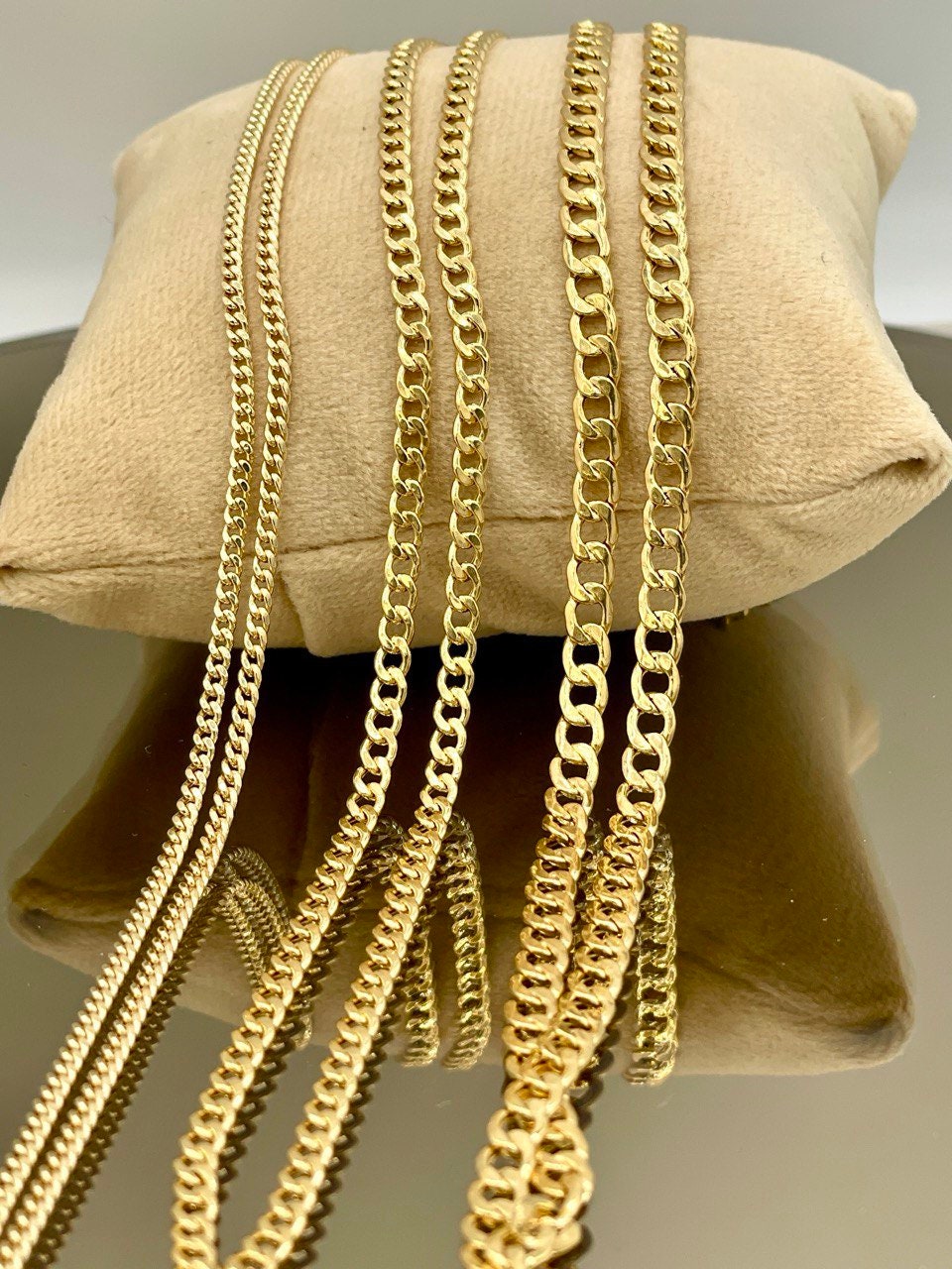 Gold chains displayed on a beige pillow with a neutral background