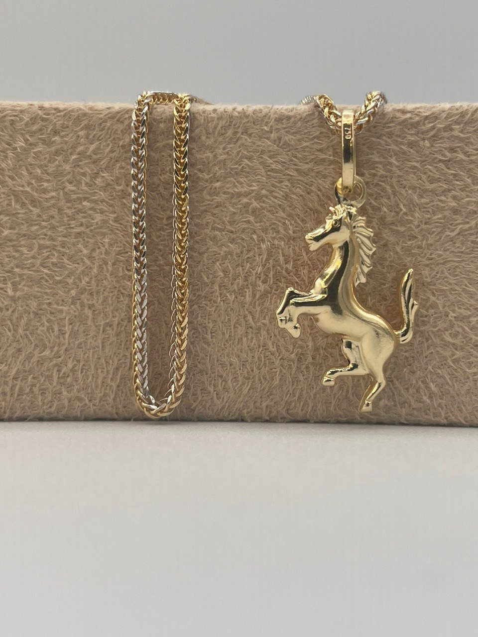 Gold horse pendant necklace on a textured beige surface