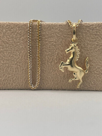 Gold horse pendant necklace on a textured beige surface