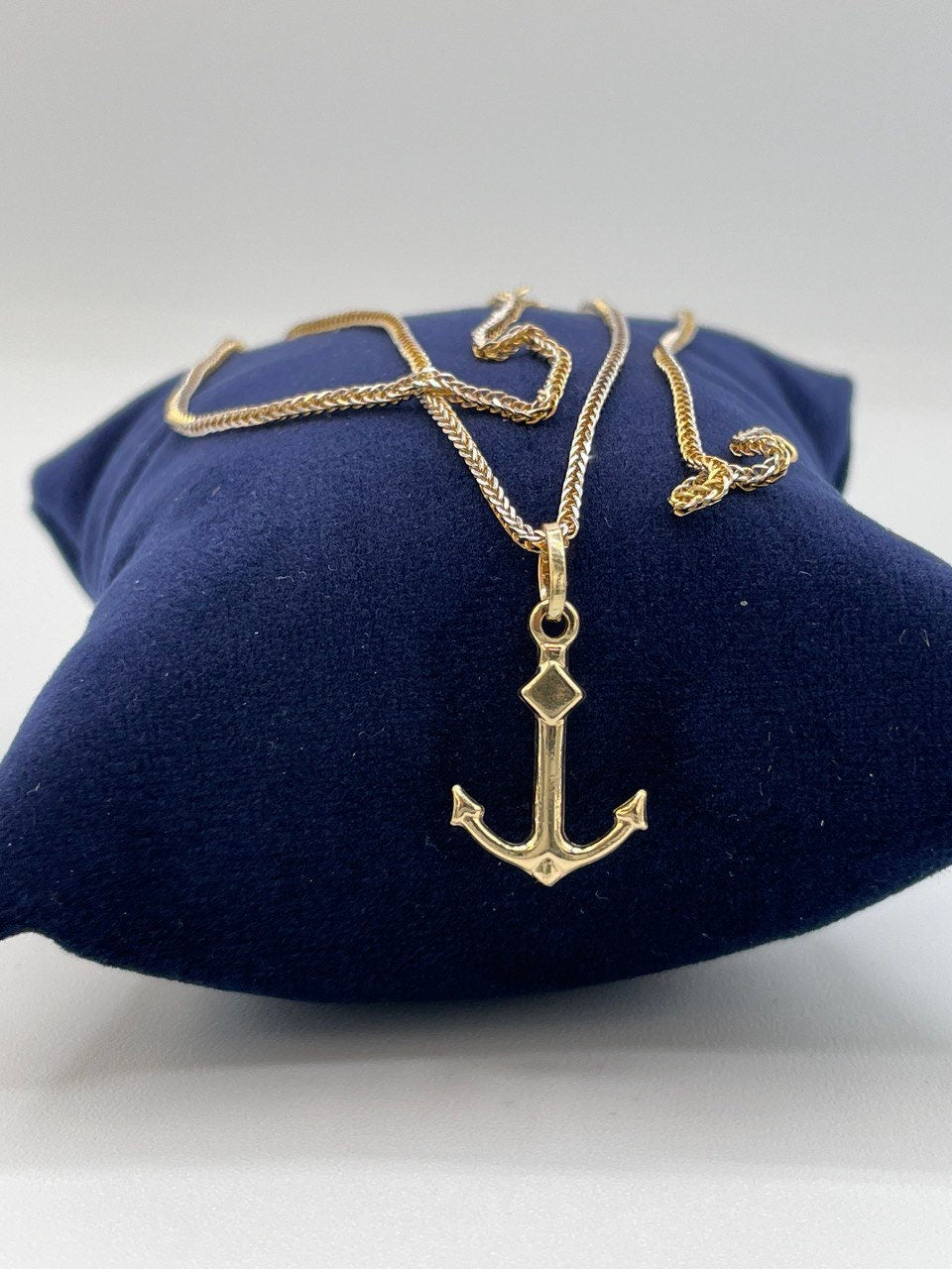 Gold anchor necklace on a blue cushion with a white background