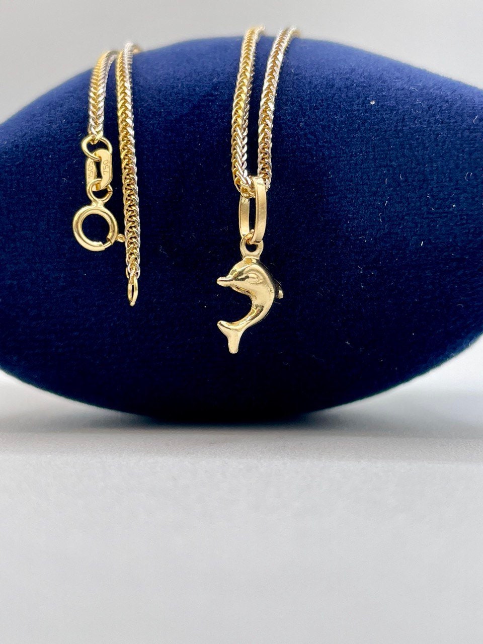Gold necklaces with dolphin pendants on a blue cushion