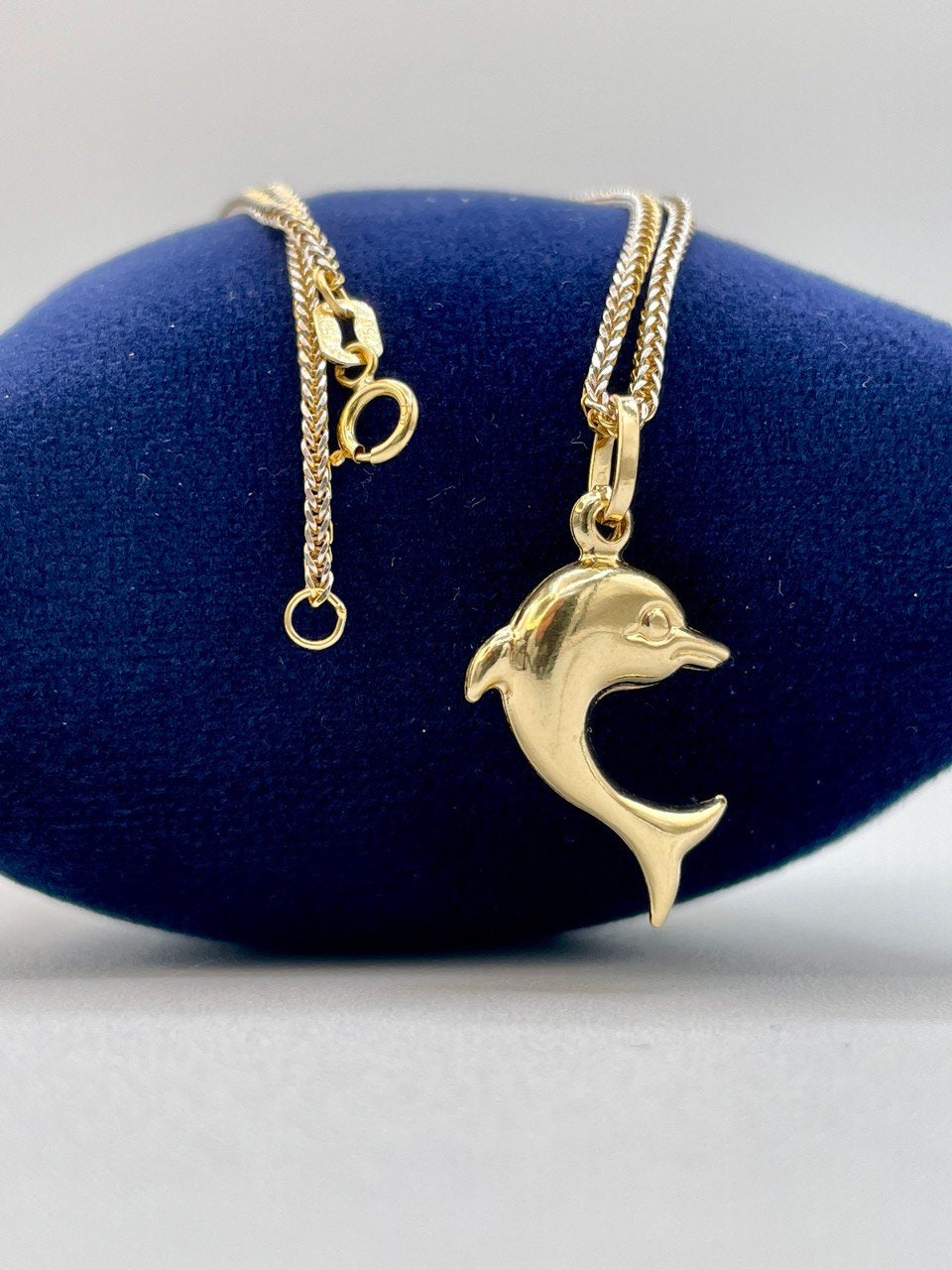 Gold dolphin pendant necklace on a blue jewelry display