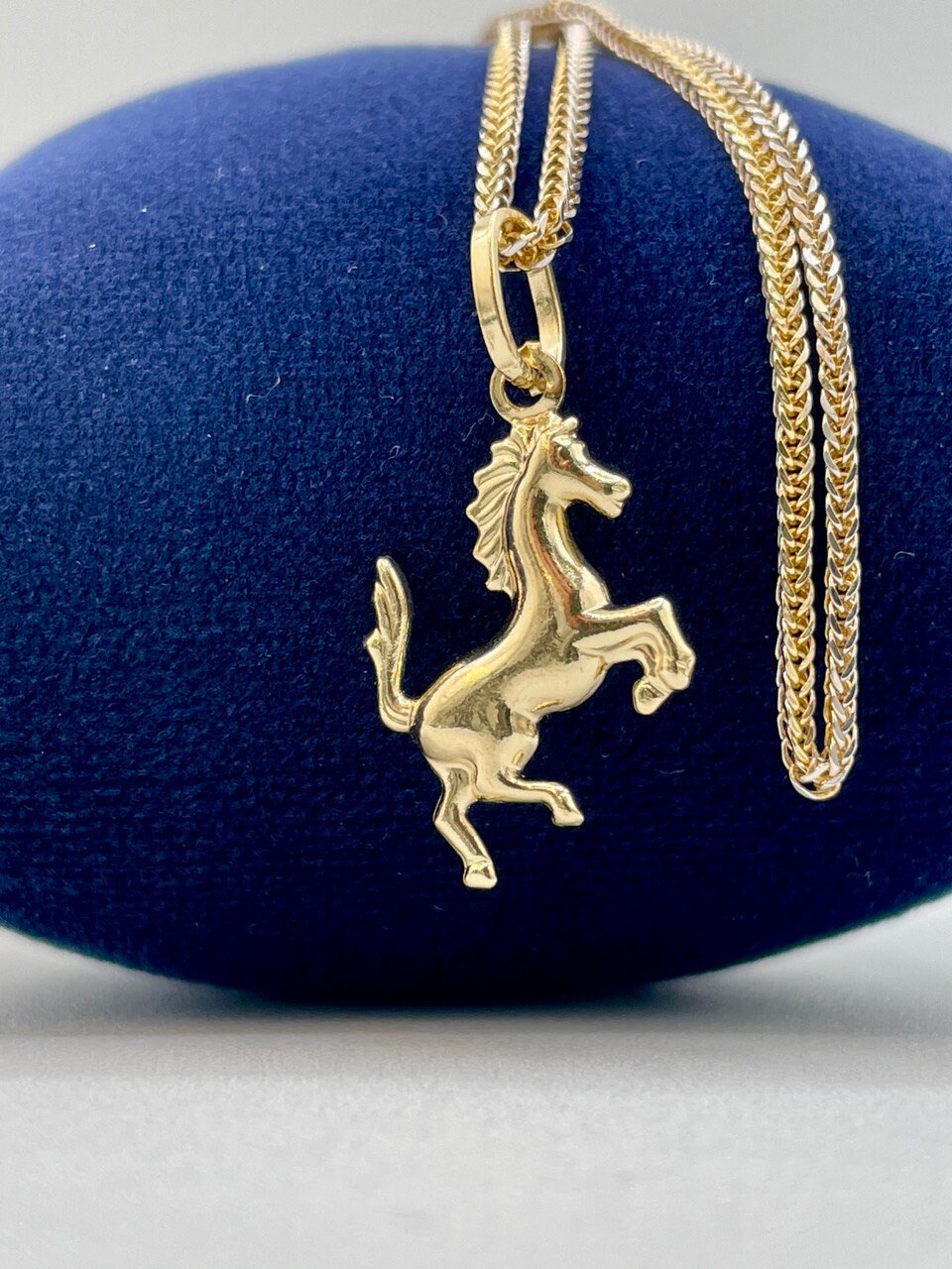 Gold horse pendant necklace on a blue cushion
