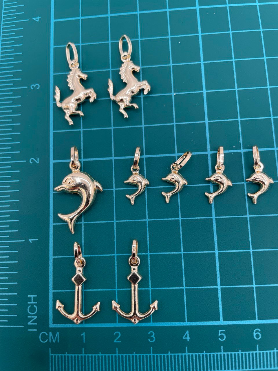 Set of silver animal and anchor pendants on a blue grid background with measurements.