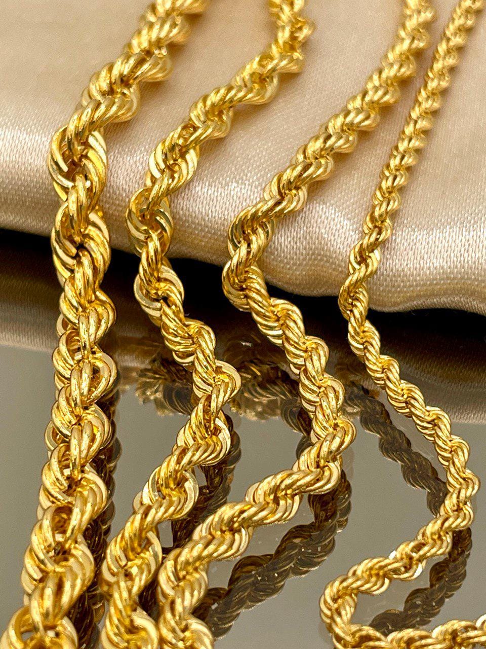 Two gold rope chains on a reflective surface with a neutral background
