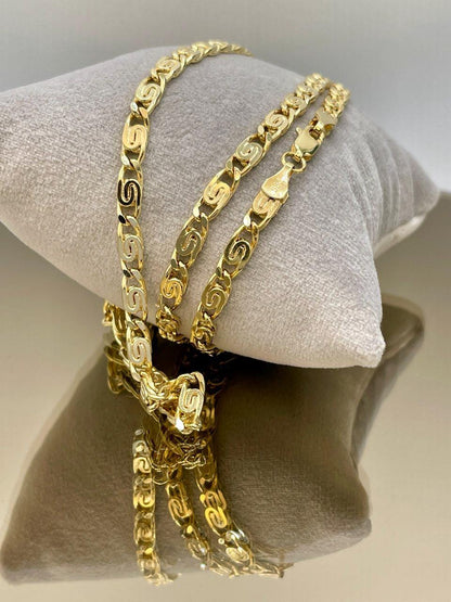 Three gold chains on a white cushion with a neutral background