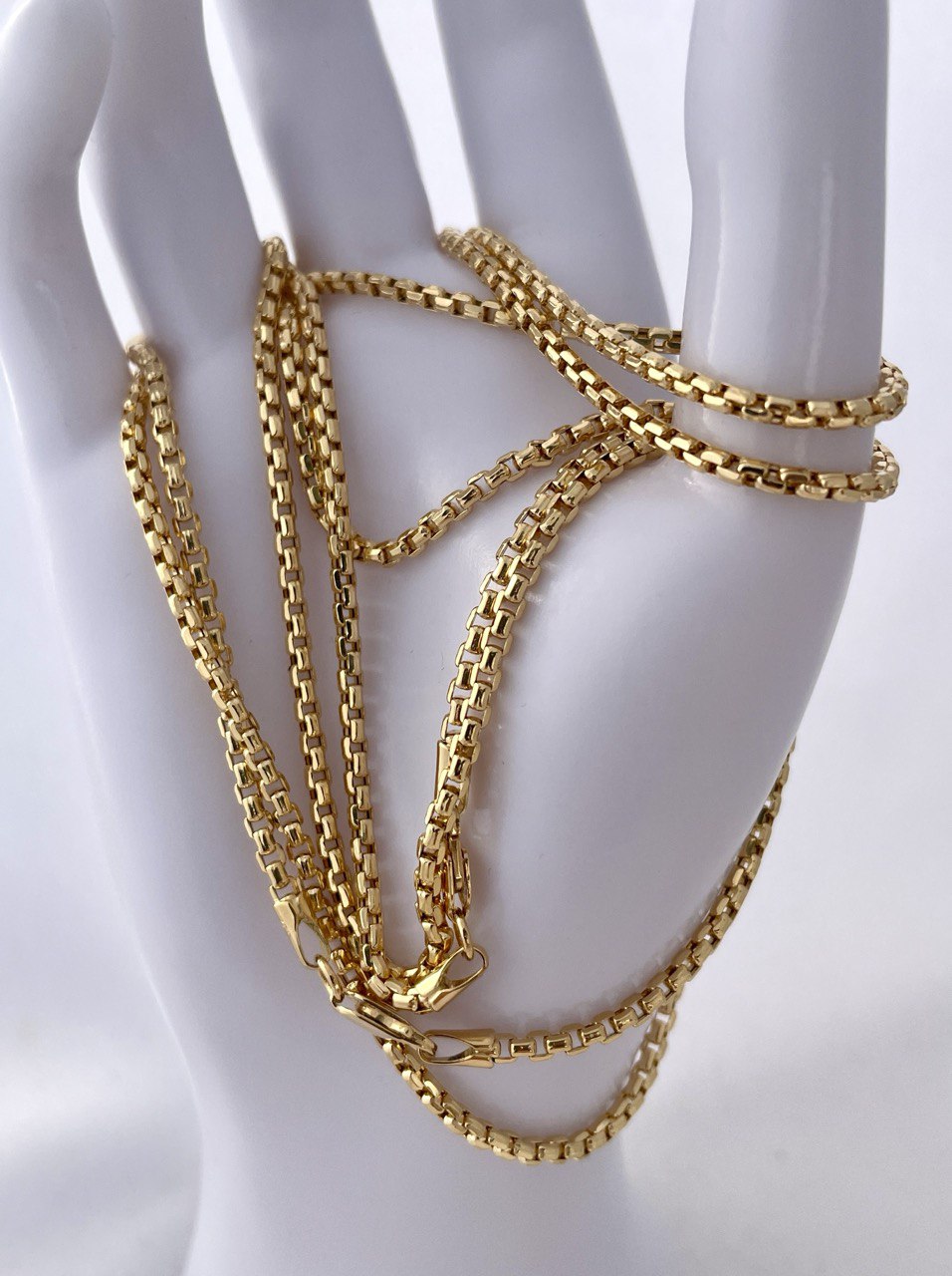 Gold chain bracelet on a mannequin arm against a white background