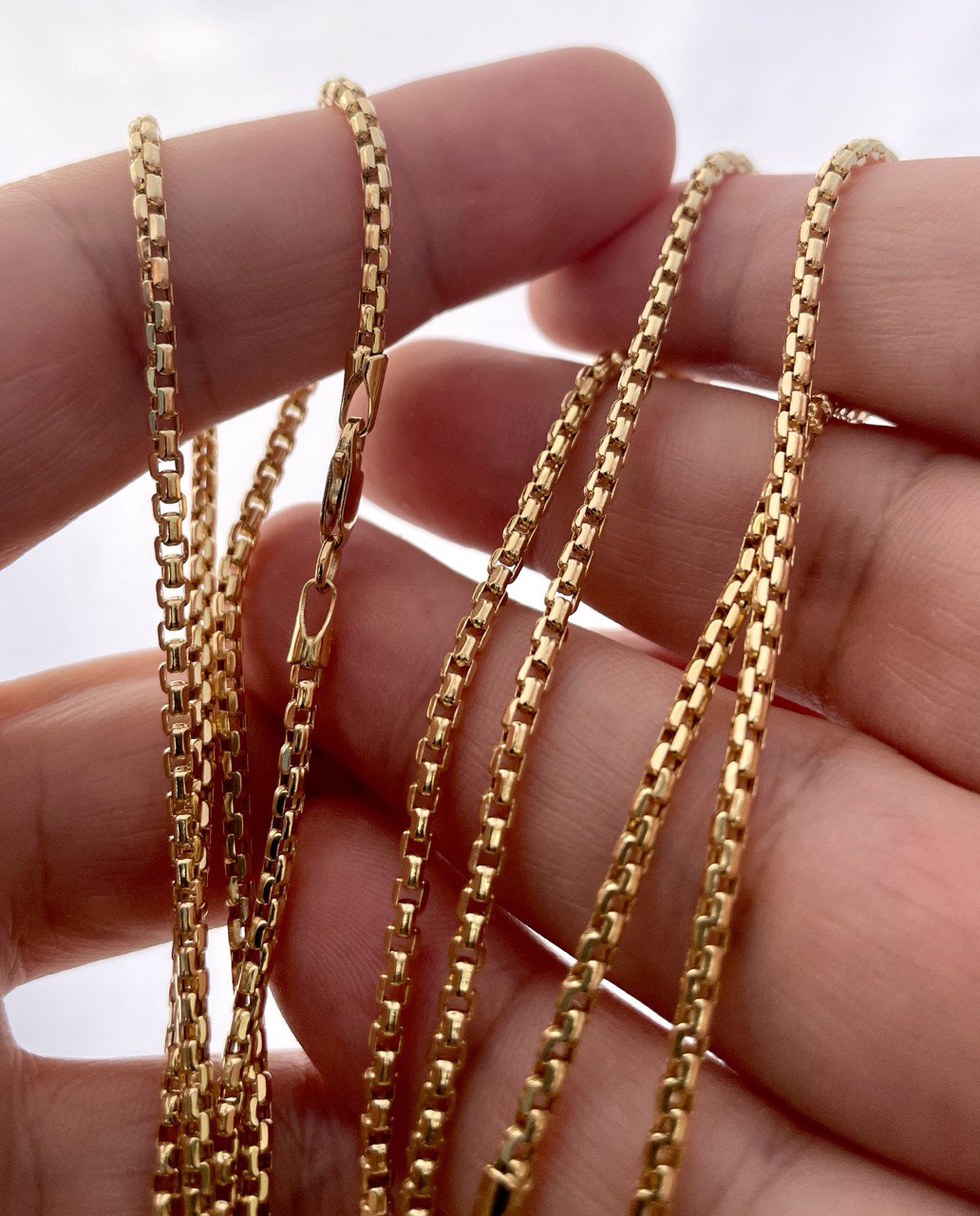 Gold chains held between fingers against a neutral background