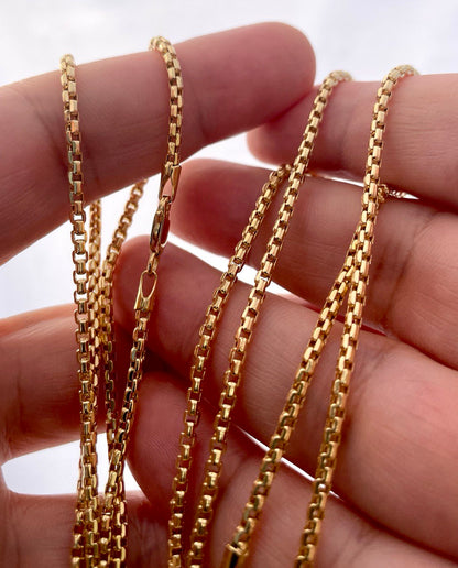 Gold chains held between fingers against a neutral background